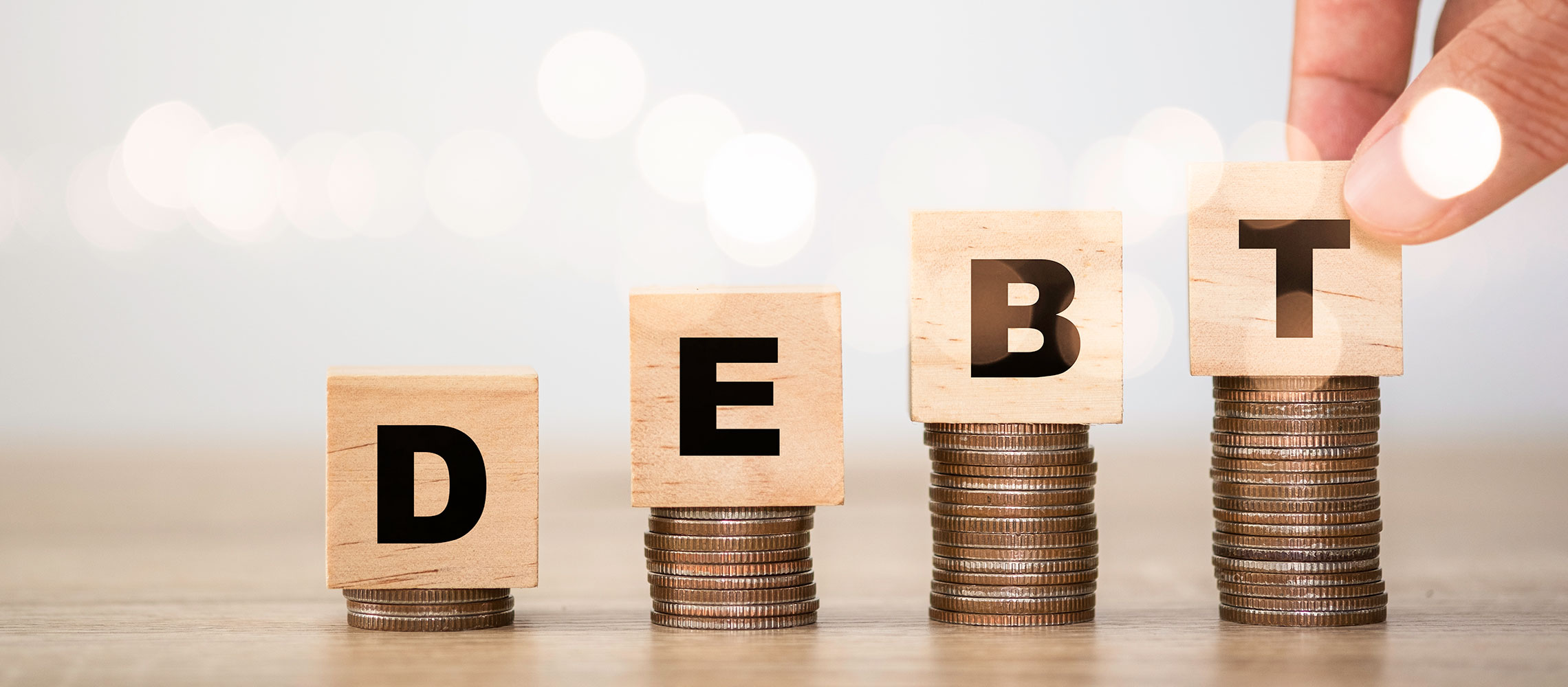 wooden blocks spelling 'debt' placed on top of stack of quarters