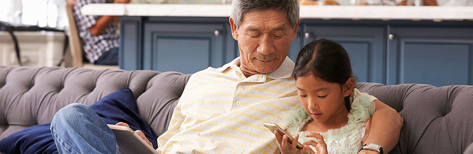 grandfather sitting with granddaughter on a couch with mobile devices in hand