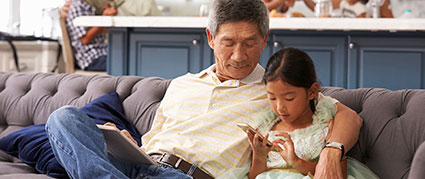 grandfather sitting with granddaughter on a couch with mobile devices in hand