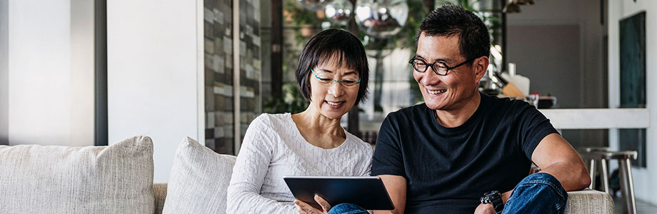 middle aged couple sitting on a couch looking at a tablet