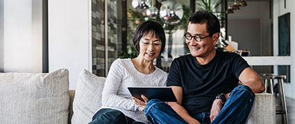 middle aged couple sitting on a couch looking at a tablet