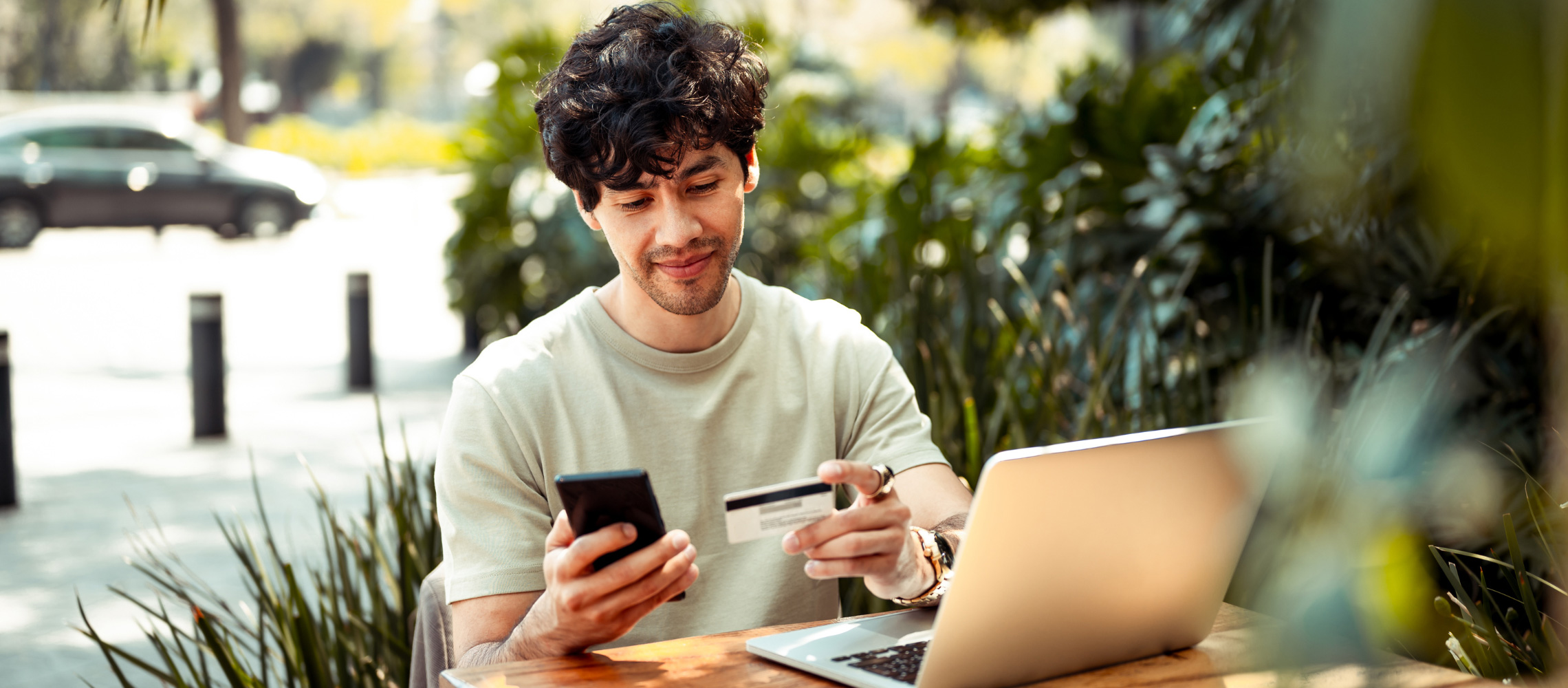 Man at table with laptop using phone with payment card