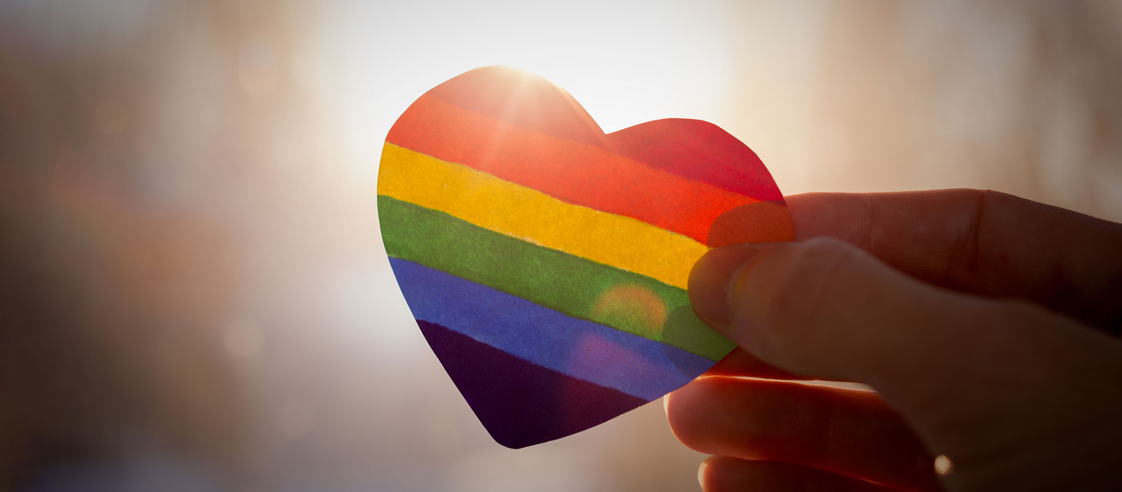 rainbow-colored paper heart being held by fingers