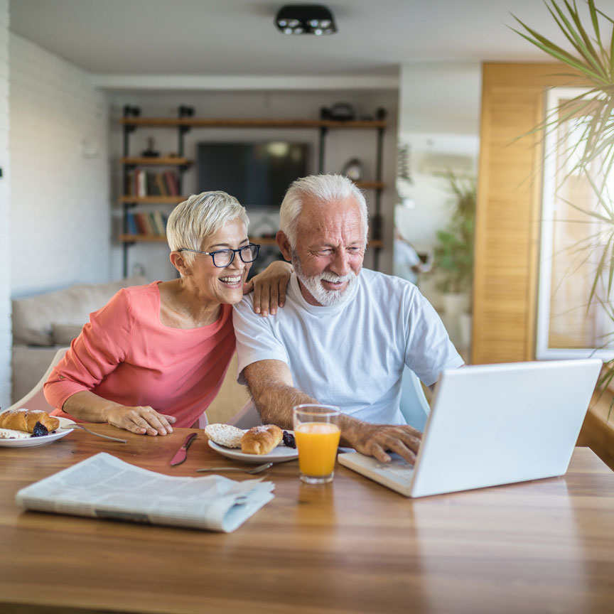 elderly couple at breakfast table with laptop