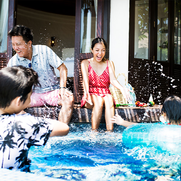 A family laughing together as they dangle their feet in a swimming pool.